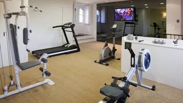 Un gimnasio en casa con máquinas de cardio, una máquina de remo y un televisor al fondo.