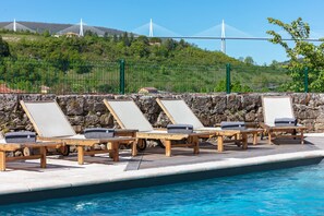 A poolside area with lounge chairs and a stone wall. - Château de Creissels (Creissels)