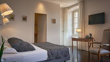 A hotel room with a bed, a desk with a chair, a TV, and a window with curtains.