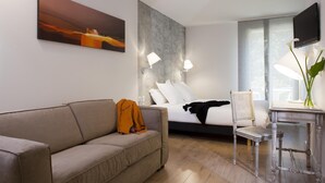 A modern hotel room with a sofa, a bed, a desk with a chair, a TV, and a painting on the wall. - Château de Creissels (Creissels)