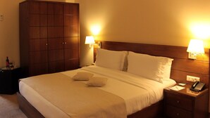 Una habitación de hotel con una cama grande, dos lámparas de noche, un armario de madera y un teléfono junto a la cama.