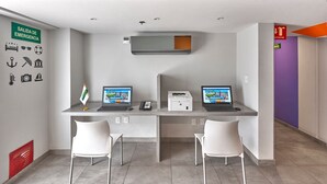 A modern office space with two desks, each with a laptop and a phone. There are two white chairs, a flag, and an emergency exit sign. - City Express Junior by Marriott Ciudad de México Zona Reforma (Mexico City)