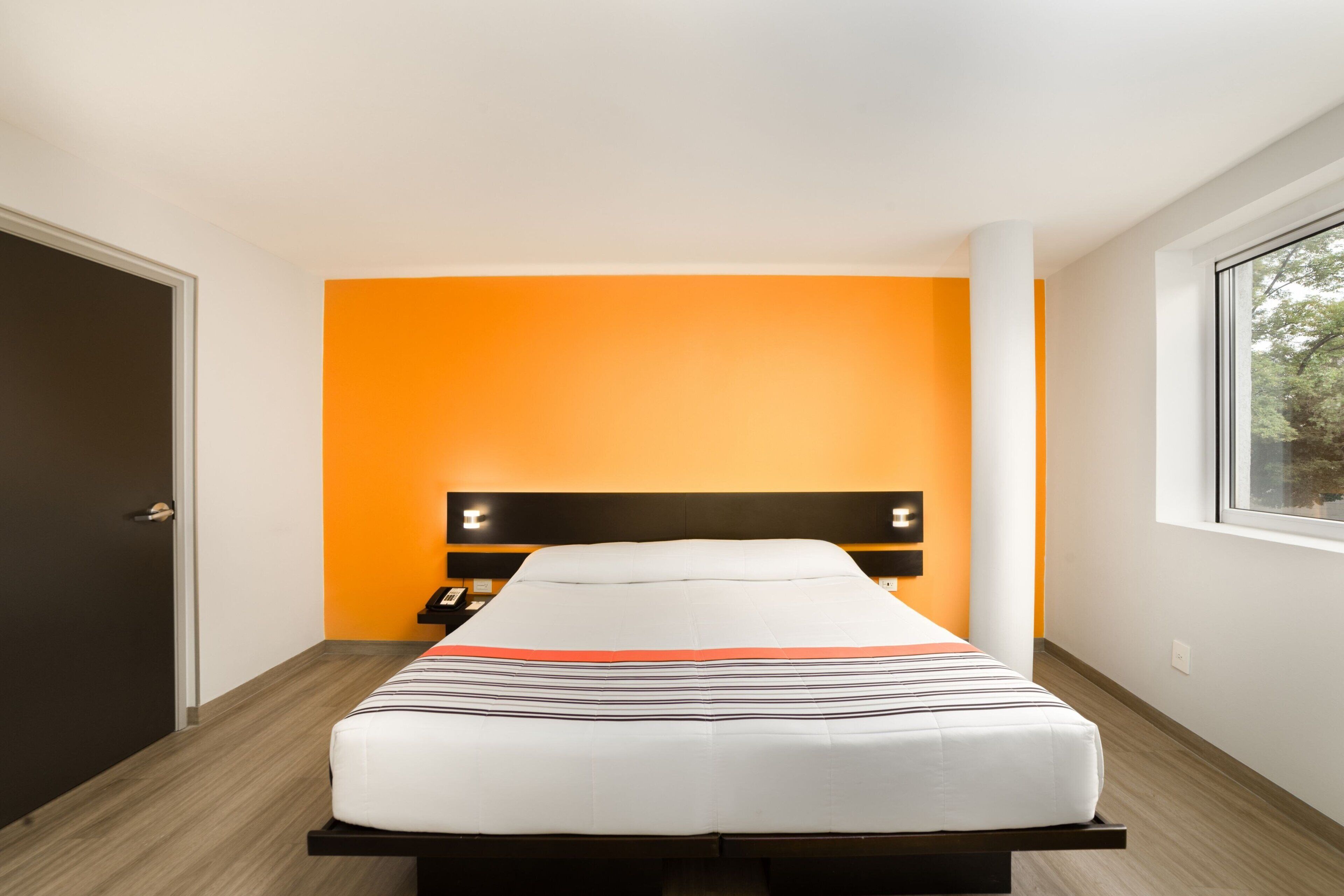 Una habitación de hotel moderna con cama, mesita de noche y ventana.
