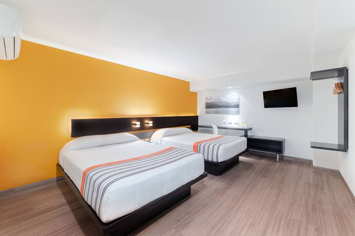 A hotel room with two beds, a desk, a TV, and a bathroom.
