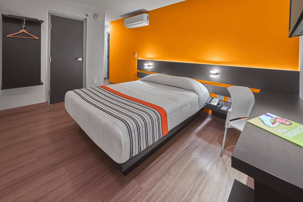 A modern hotel room with a bed, bedside table, chair, and a desk with a magazine.