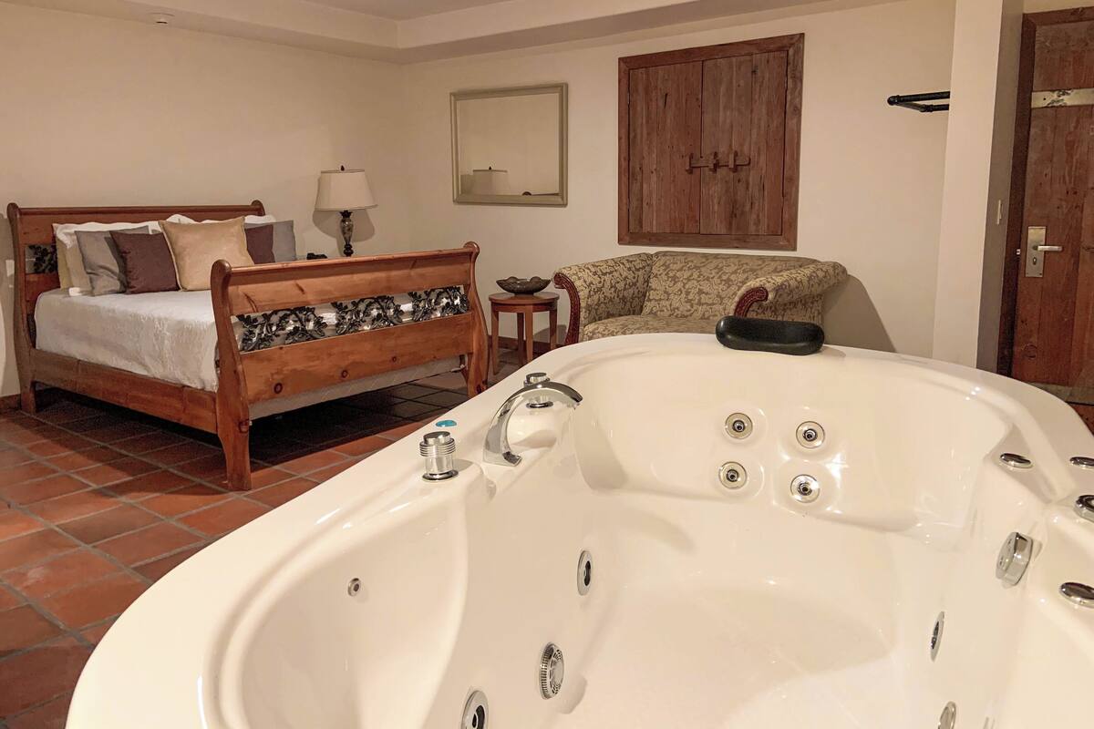 Une chambre à coucher avec un lit en bois, une grande baignoire blanche, un canapé à motifs et une armoire en bois.