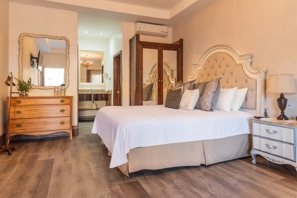 A bedroom with a large bed, wooden dresser, and a mirror. - Hotel Hacienda Santana (Tecate)