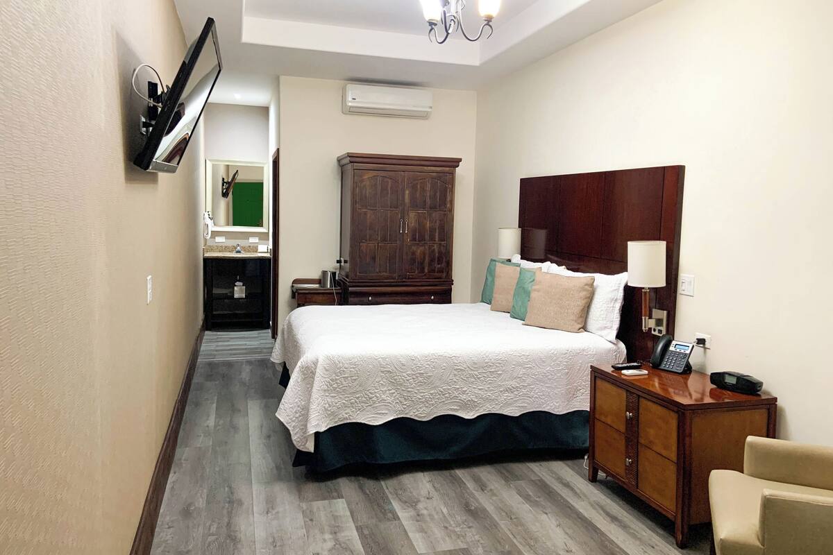 Une chambre d’hôtel avec un grand lit, une armoire en bois, une table de chevet avec une lampe et un téléphone.