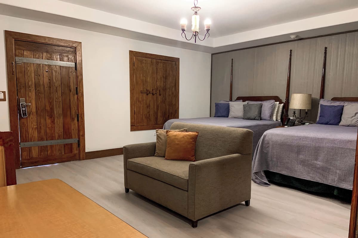 Une chambre d’hôtel avec deux lits, une armoire en bois, un canapé et une table à manger.