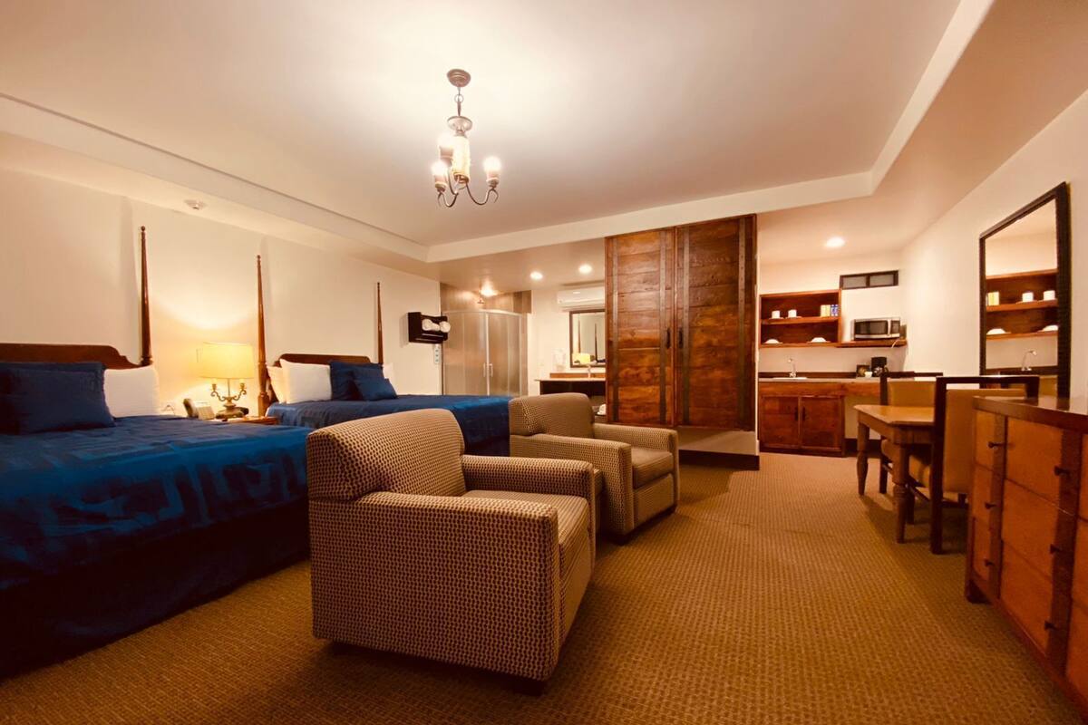 Une chambre d’hôtel comprenant un lit, deux fauteuils, un bureau, une kitchenette et une armoire.