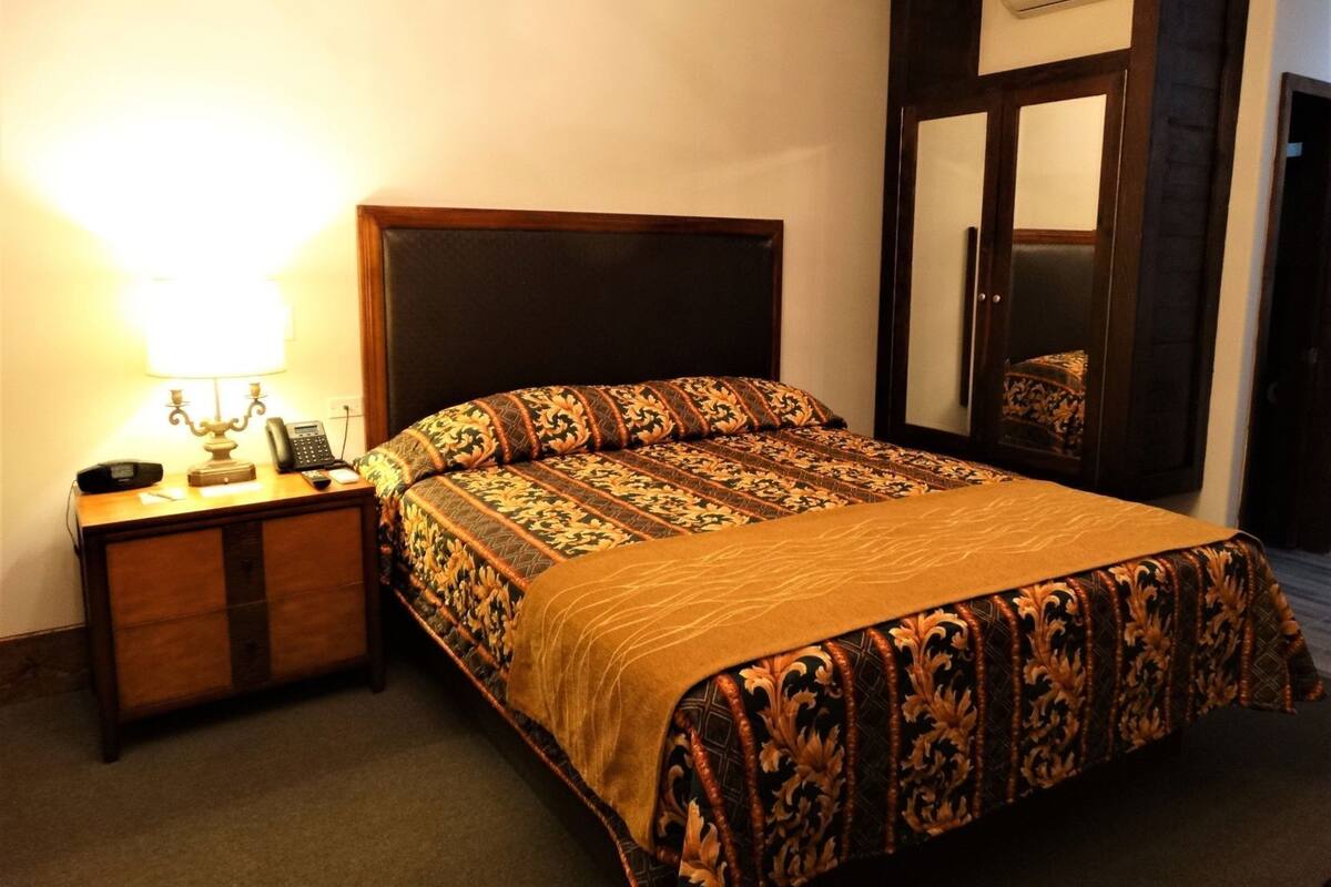 Une chambre d’hôtel comprenant un lit, une table de chevet avec une lampe, un téléphone et un miroir.