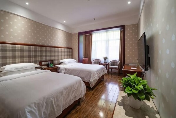 Camera d'albergo con due letti, una televisione, una scrivania, una sedia, una finestra con tende e una pianta in vaso.
