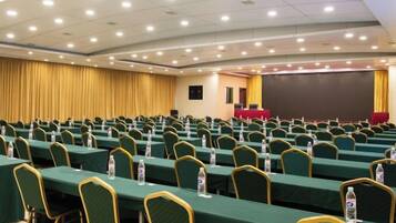 A conference room with rows of tables and chairs, a stage, and a projection screen.