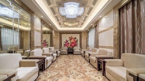 Une salle de conférence d’hôtel dotée d’un sol en marbre, de canapés beiges et d’un arrangement floral en guise de décoration centrale.