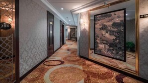 Un couloir avec un tapis à motifs, une grande œuvre d’art encadrée et un panneau indiquant un numéro de porte sur le mur.