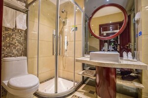 Un baño con ducha envuelta en vidrio, inodoro, lavabo con espejo y tocador con artículos de aseo.
