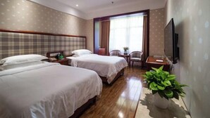 Habitación de hotel con dos camas, televisión, planta y ventana con cortinas.