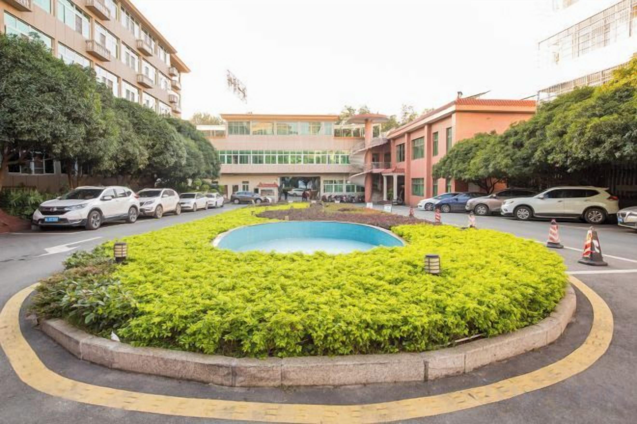 A roundabout with a central landscaped area, surrounded by multi-story buildings, and parked cars along the roadside.