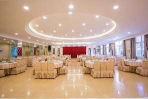 A large banquet hall with round tables and chairs, a stage with a red backdrop, and a high ceiling with recessed lighting. - Ganzhou Hotel (Ganzhou)