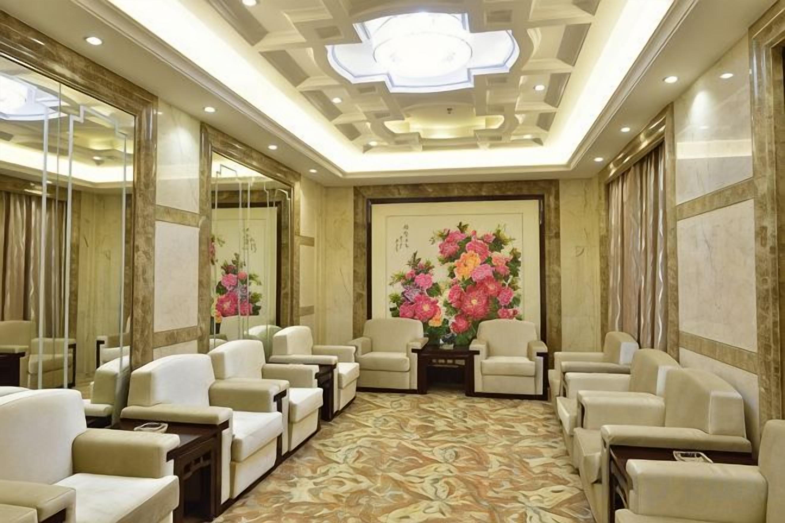A hotel lobby with a patterned carpet, seating area with chairs, and a large floral painting on the wall.