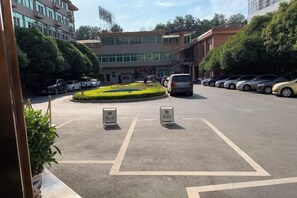 A parking lot with marked spaces, a landscaped area, and a building with multiple floors in the background. - Ganzhou Hotel (Ganzhou)