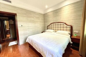 A hotel room with a large bed, wooden headboard, and a nightstand with a lamp. - Ganzhou Hotel (Ganzhou)