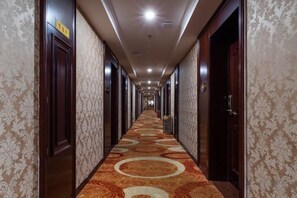 A hotel corridor with patterned wallpaper, wooden doors, and a carpeted floor. - Ganzhou Hotel (Ganzhou)