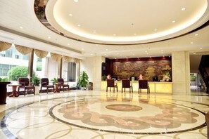 Una hall d'albergo con reception, area salotto e un ampio pavimento circolare decorato.