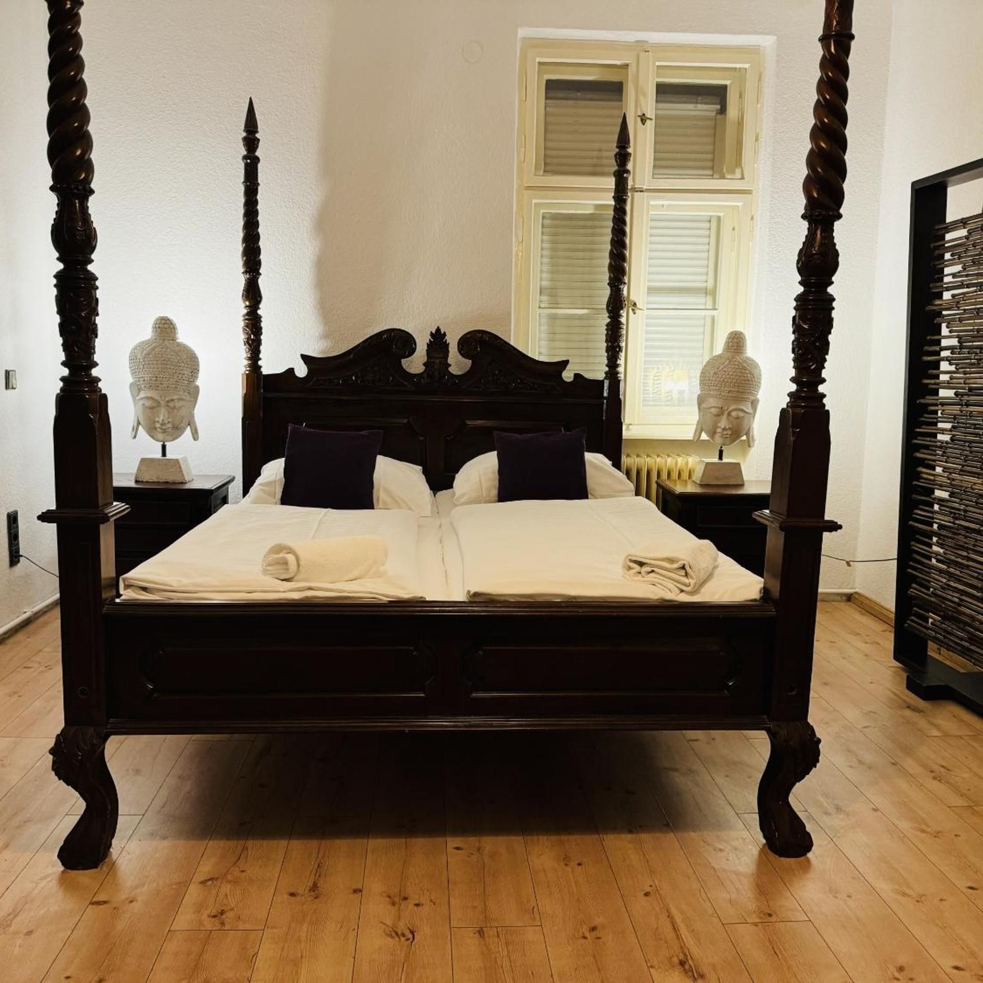 A four-poster bed with a dark finish, white bedding, and two nightstands with sculptures.