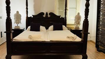 Una cama con dosel de cuatro postes con terminación oscura, ropa de cama blanca y dos mesitas de noche con esculturas.
