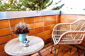 A round table with a potted plant and a bottle, a wicker chair, and a tiled wall. - Hotel Nest (Berlin)