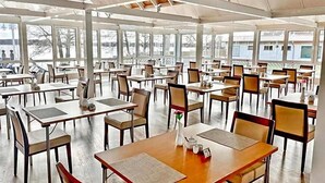 A spacious indoor dining area with multiple tables and chairs, large windows, and a high ceiling.