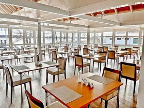 A spacious indoor dining area with multiple tables and chairs, large windows, and a high ceiling.