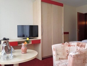 A hotel room with a television, a small table with a vase, and a sofa.