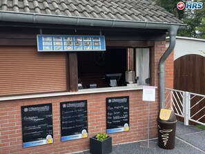 Ein Backsteinhaus mit heruntergelassener Rollläde, einer Speisekarte und einem Mülleimer.