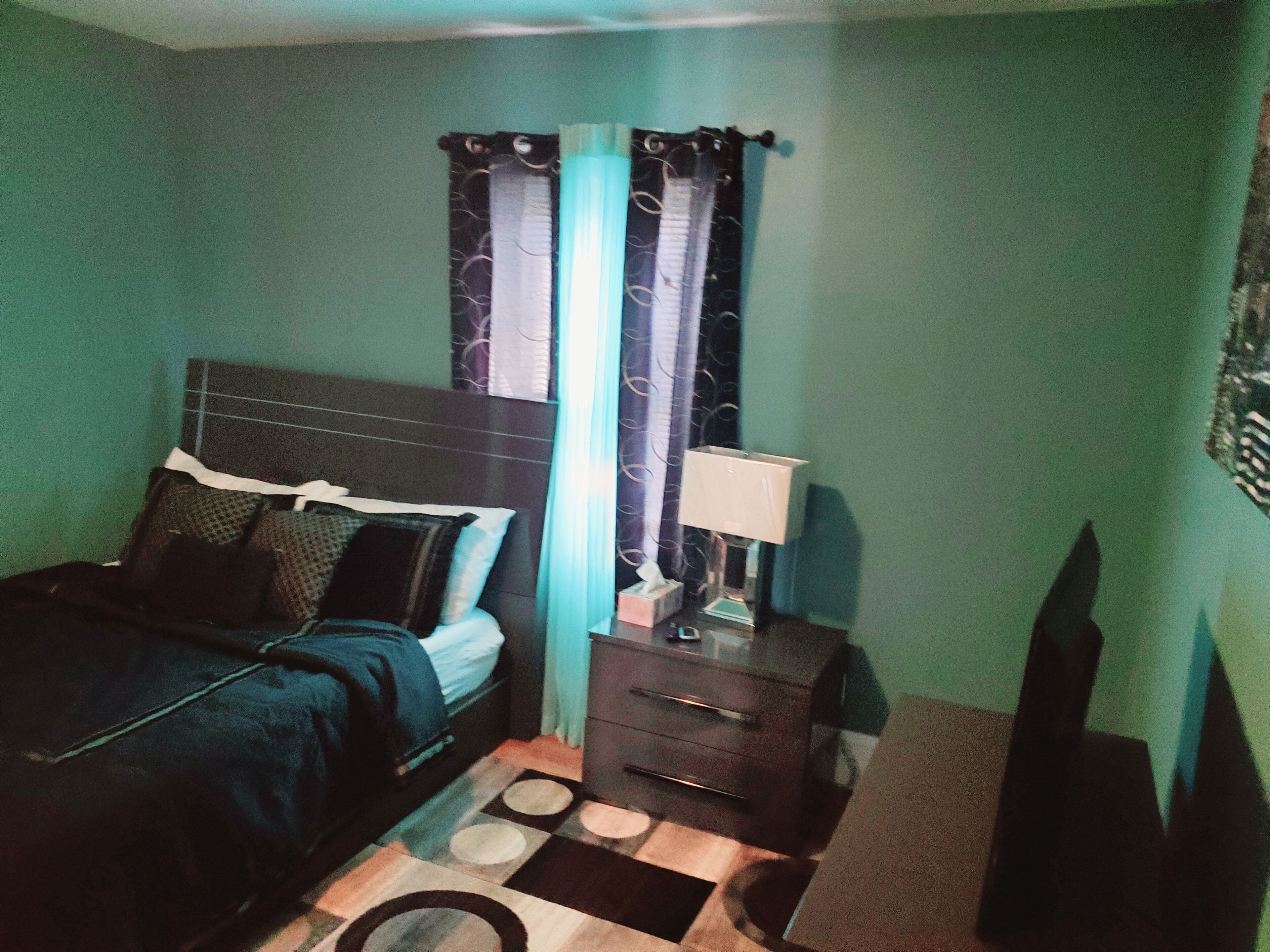 A bedroom with a bed, a nightstand, a lamp, and a window with curtains.