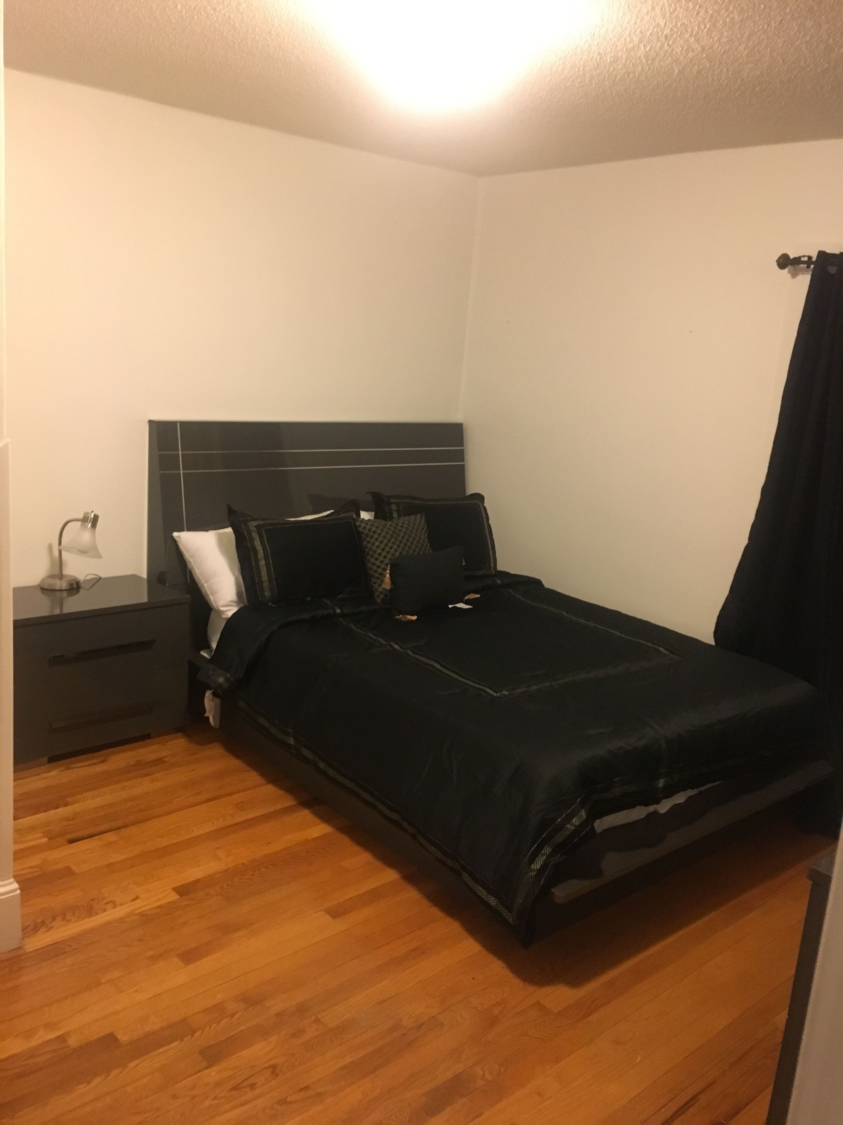 Ein Schlafzimmer mit Bett, Nachttisch, Lampe und Vorhang.