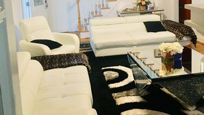 A living room with white sofas, a black and white rug, a staircase, and a coffee table with decorative items. - Upscaled Home in a Quiet Neighborhood (Springfield)
