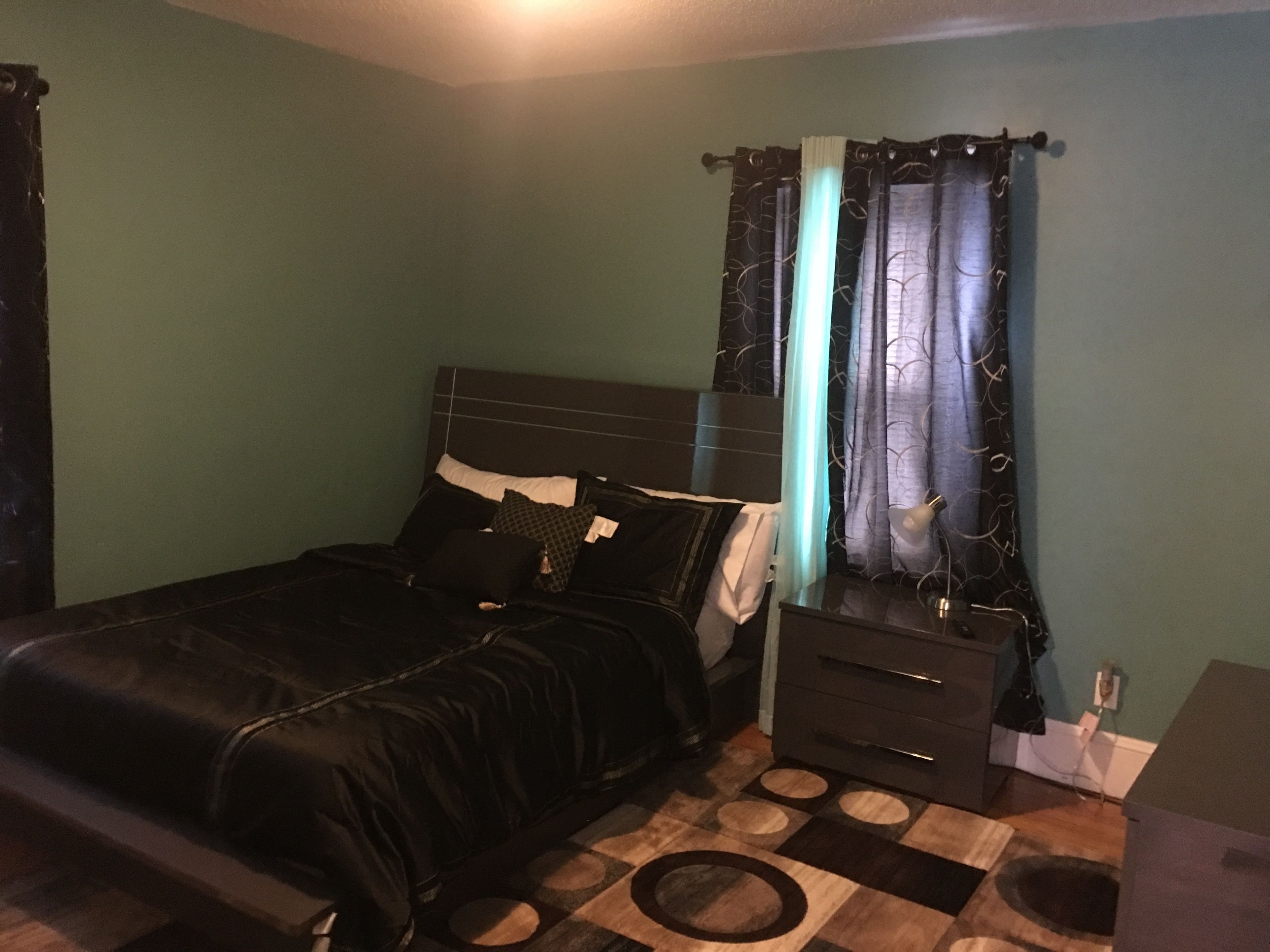 A bedroom with a bed, a nightstand, a lamp, and a window with curtains.