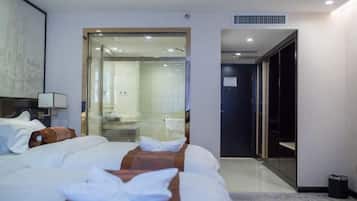 Una habitación de hotel con una cama grande, un baño visible a través de una puerta de cristal y un armario.