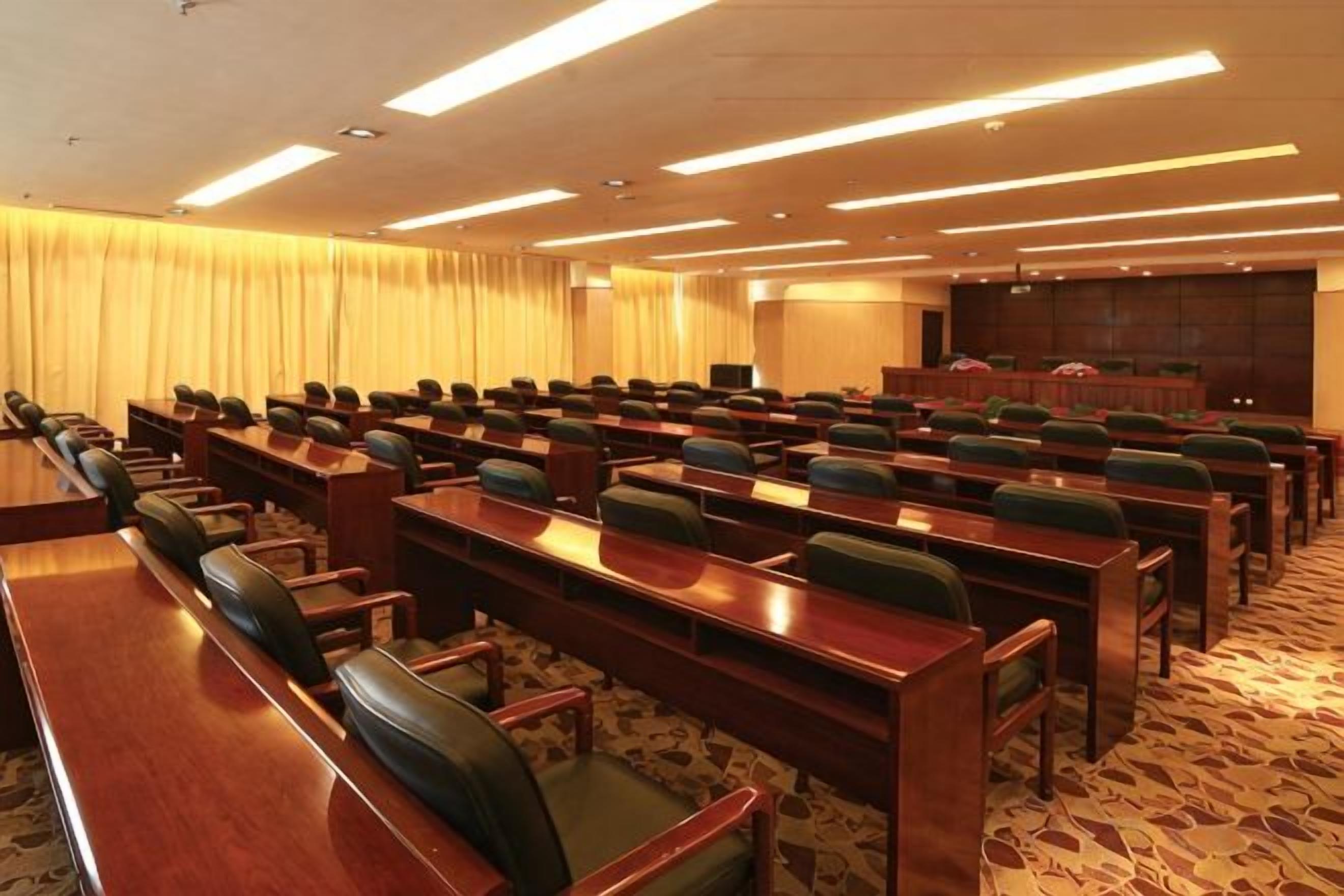 A conference room with rows of tables and chairs, a stage, and a carpeted floor.
