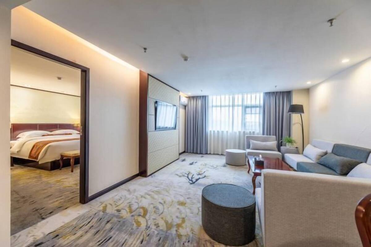 A hotel room with a bed, a sofa, a coffee table, a lamp, and a window with curtains.