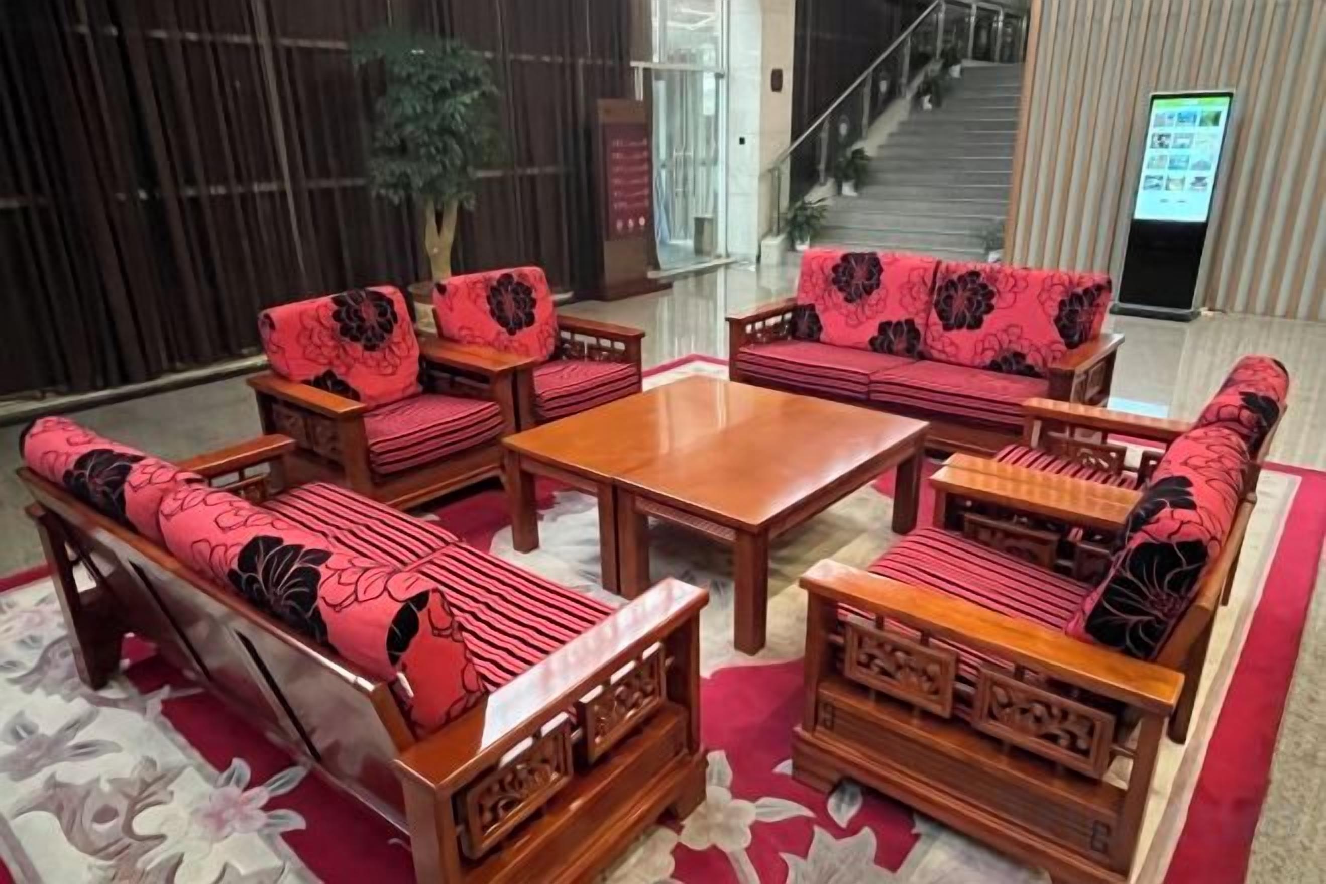 A hotel lobby with a seating area featuring sofas and chairs with floral upholstery, a wooden coffee table, and a red carpet.