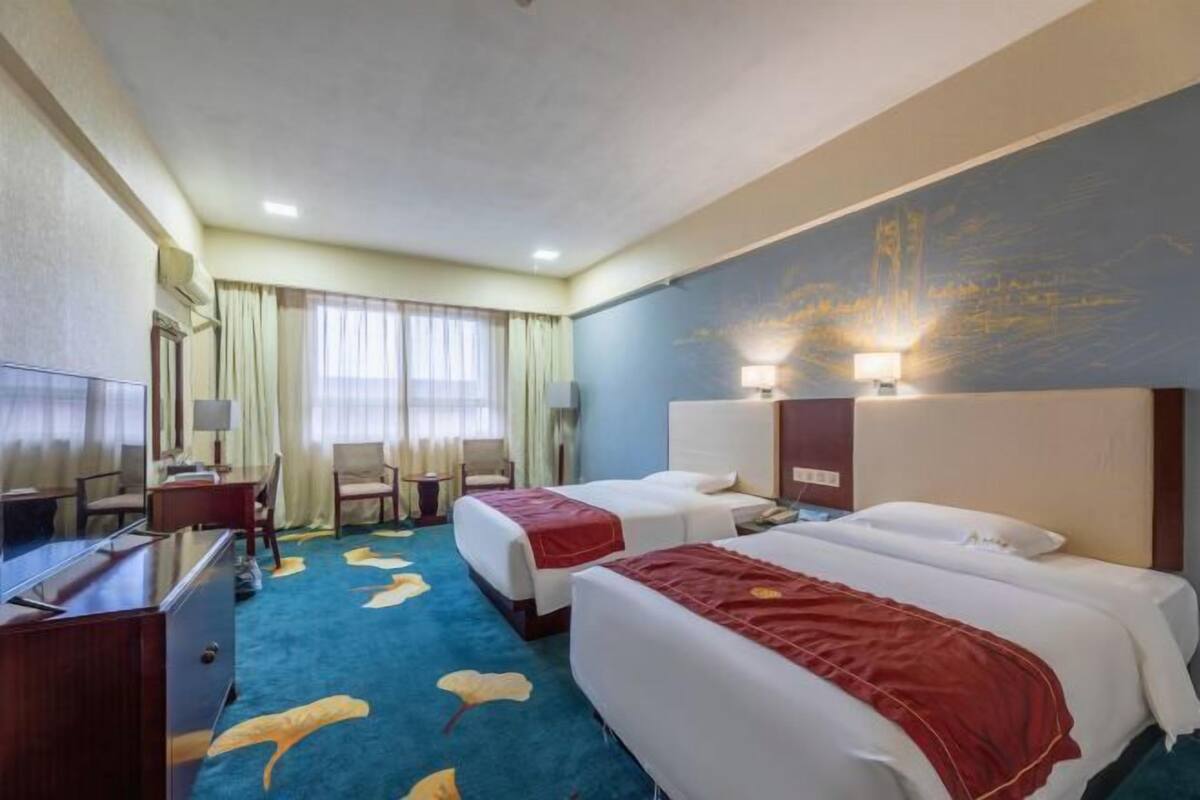 A hotel room with two beds, a desk, a chair, and a large window with curtains.