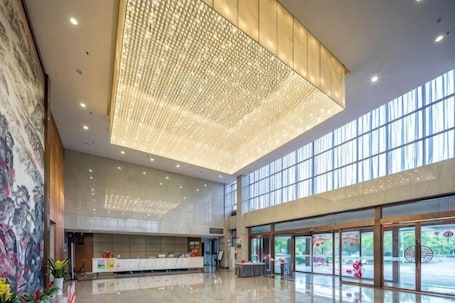 A spacious lobby with a high ceiling, a reception desk, and large windows allowing natural light.. Jiangxi Bailu Hotel
