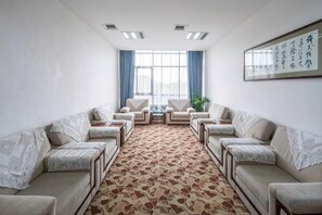 A conference room with a patterned carpet, two sofas facing each other, a table, and a window with curtains. - Jiangxi Bailu Hotel (Nanchang County)