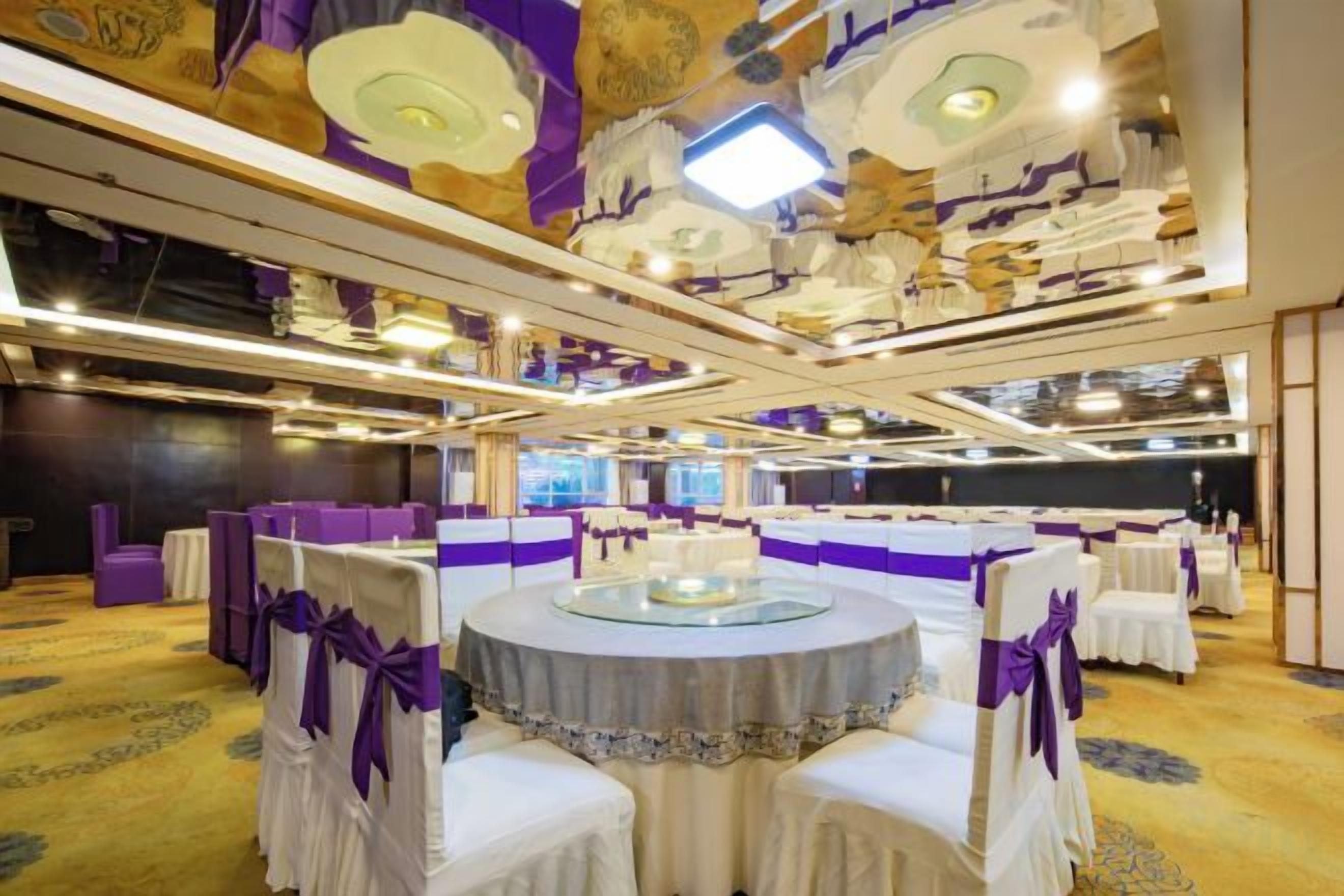A banquet hall with round tables, purple decor, and a high ceiling with ornate lighting fixtures.
