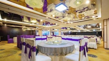 Un salón de banquetes con mesas redondas, decoración morada y un techo alto con candelabros ornamentales.