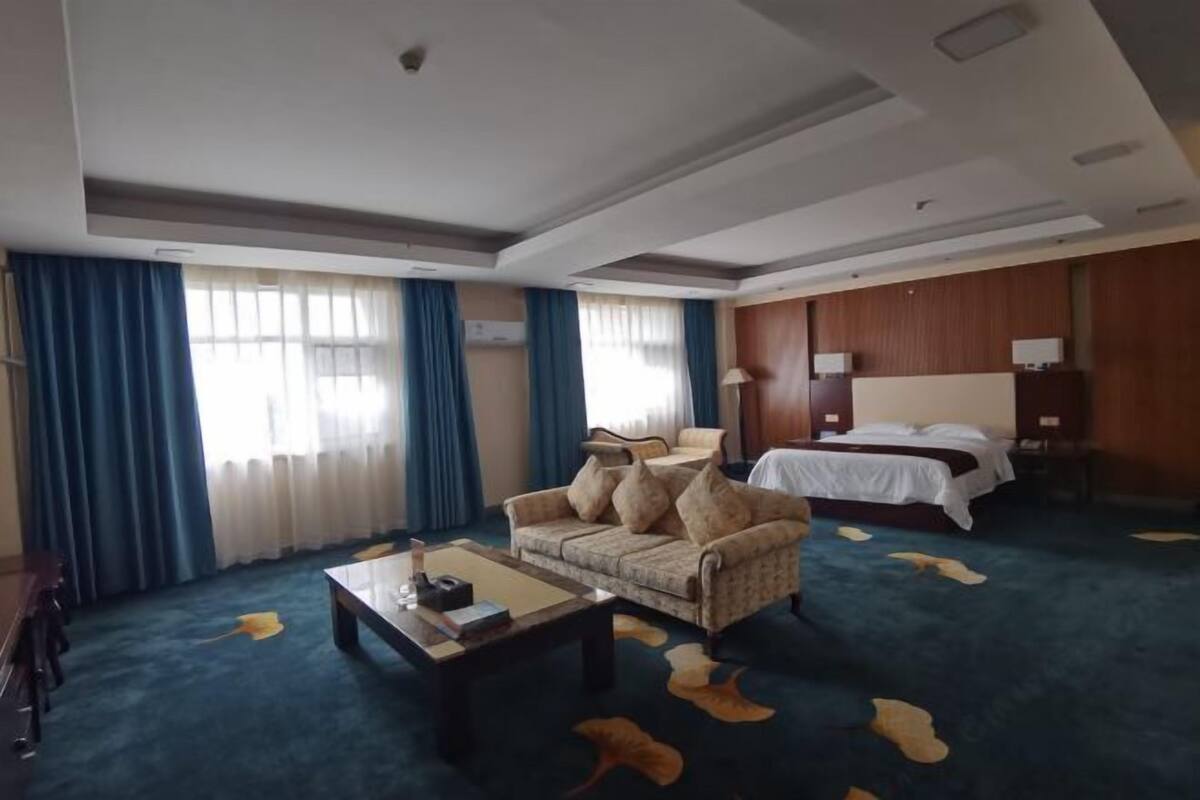 A hotel room with a sofa, a bed, a coffee table, and a carpet with animal prints.