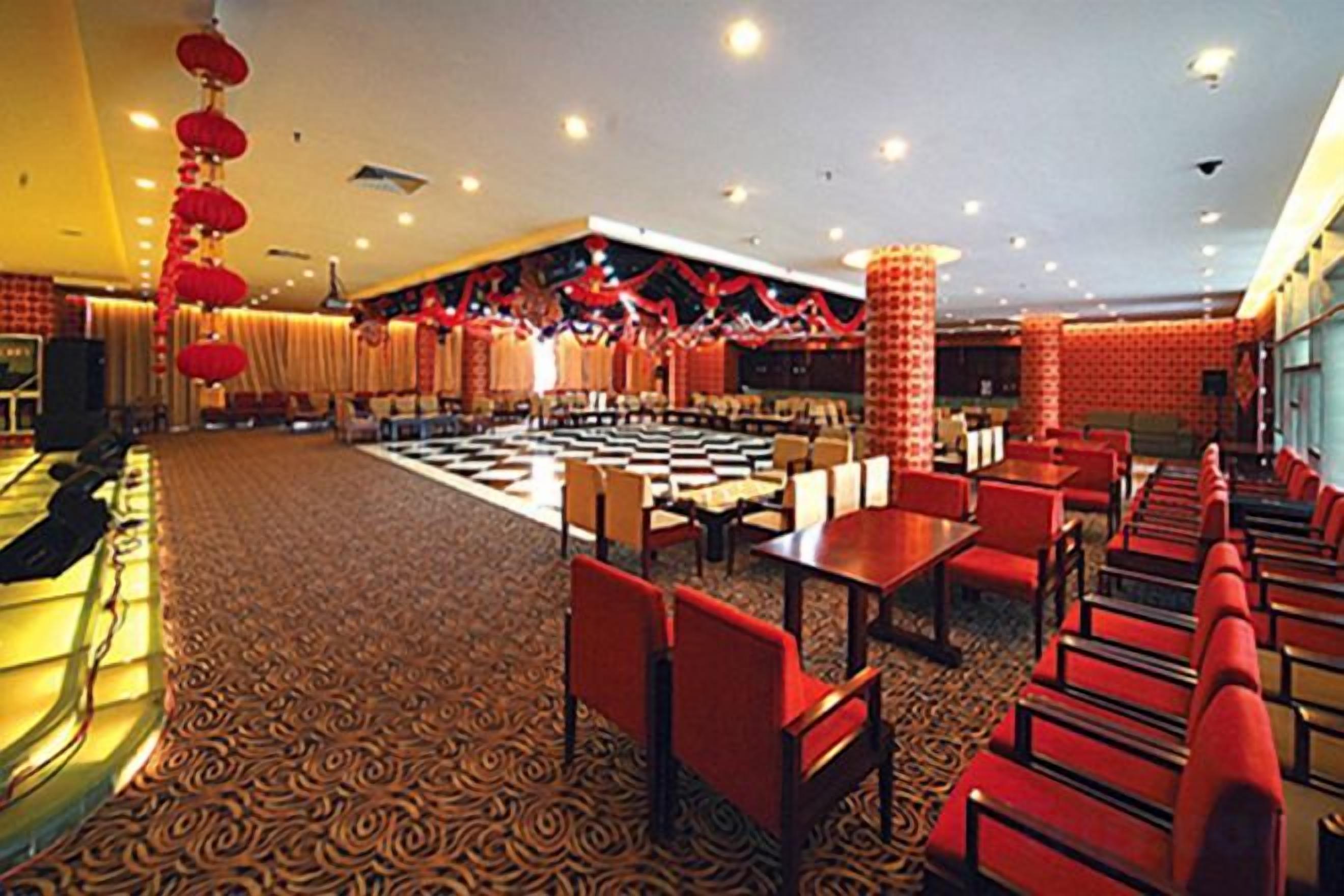 A hotel lobby with a checkered floor, red seating, and a central area with tables and chairs.